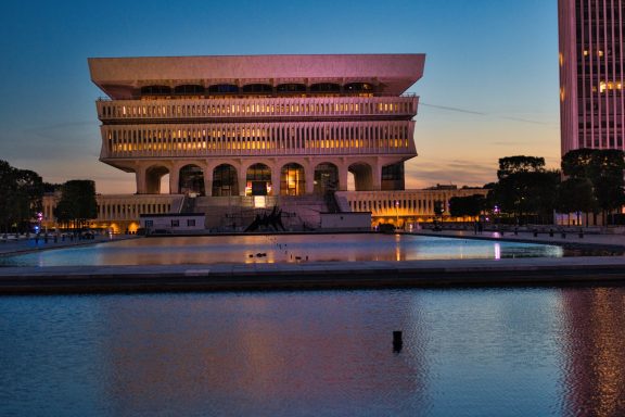Bldg reflecting in water Modern building reflecting in water at dusk, with colorful lighting and surrounding trees.