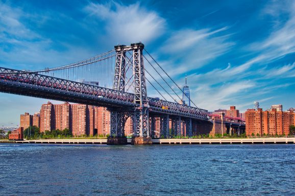 NYC Bridge Williamsburg Bridge spanning a river with buildings in the background under a blue sky.