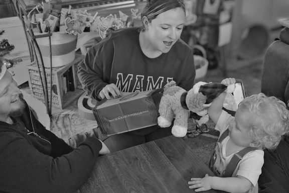 Birthday Party gift opening A woman shows a child a toy while another adult watches, all seated at a table.